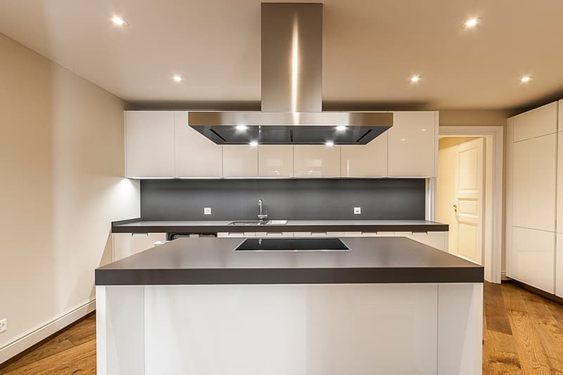 Modern kitchen with white cabinets, dark countertops, stainless steel range hood, and hardwood floors