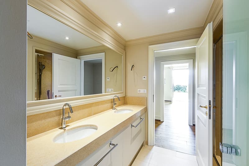 Spacious bathroom with double vanity sinks, large mirror, and a view of the hallway through the open doorway.