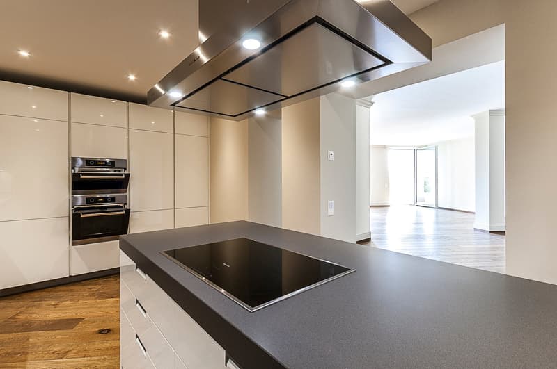 Modern kitchen with sleek white cabinets, black countertop, built-in oven and dishwasher, and an open floor plan leading to a living area
