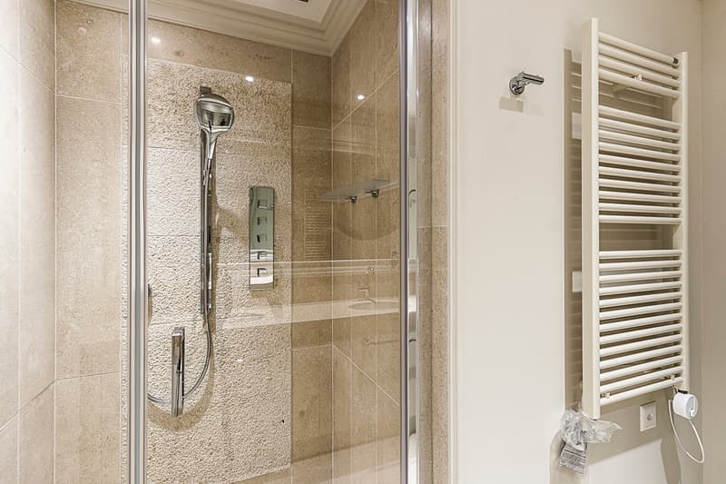 Spacious bathroom with beige tile walls, glass shower enclosure, wall-mounted towel warmer, and a shower head fixture.