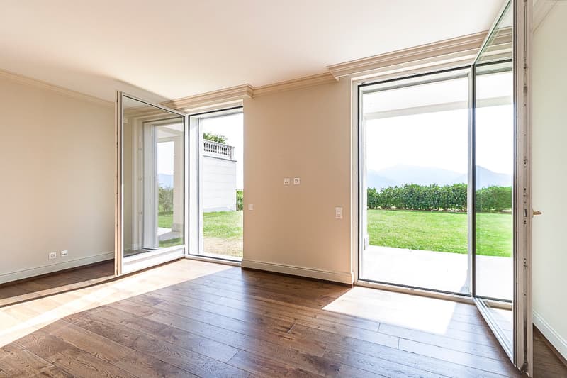 Spacious living room with large windows overlooking a grassy outdoor area, hardwood flooring, and neutral-colored walls.