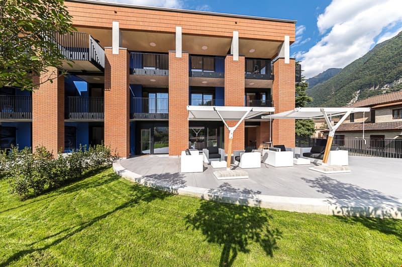 3-story brick apartment building with balconies, outdoor seating area, and landscaped grounds