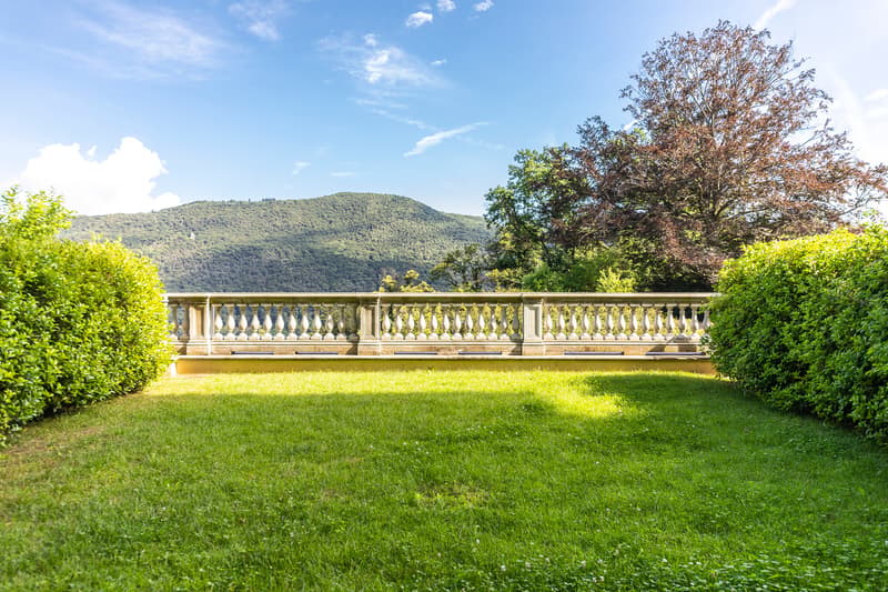 large green grass field, concrete railing, bushes, mountains in the distance