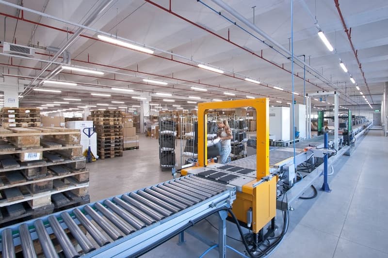 Large industrial warehouse with shelving units, conveyor belts, and a forklift operating in the center of the space.