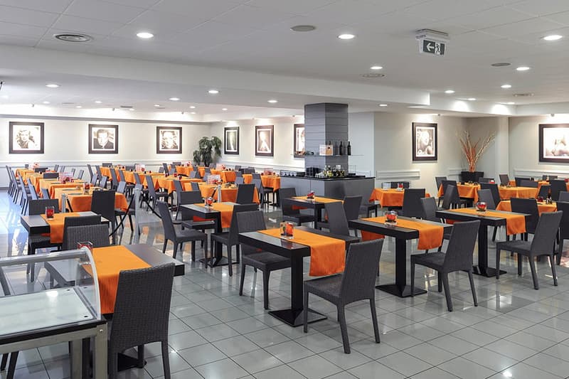 Large dining area with black and orange tables and chairs, tile flooring, wall decor, and a kitchen area with a dishwasher visible