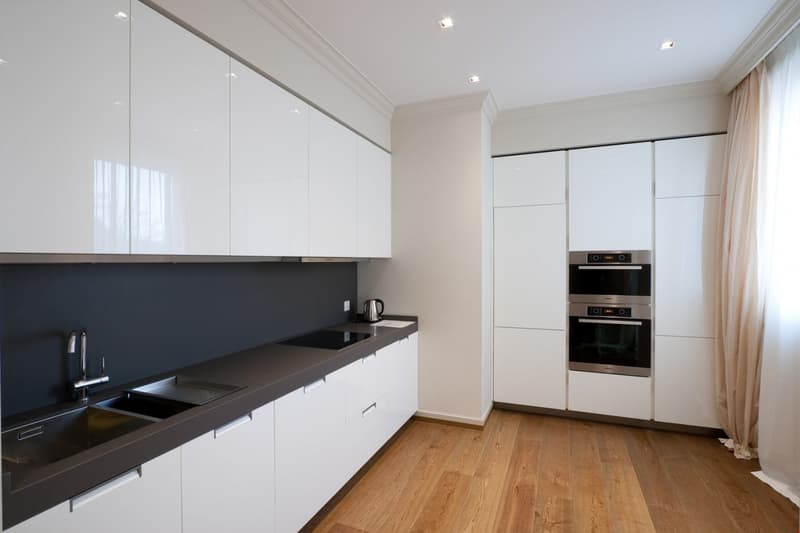 Modern kitchen with black and white colors, double ovens, granite countertop, stainless steel sink with faucet, wooden floor.
