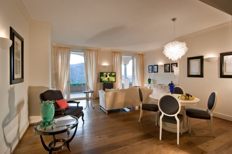 wooden floor, windows, sofa, armchair, dining table with chairs, side table, TV, paintings on wall