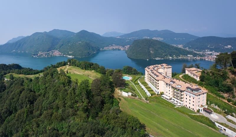 Hilltop building complex with pool, lake, mountains, and town in the distance.