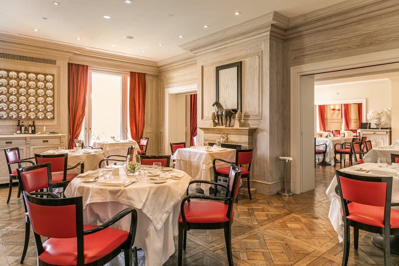 Wooden floor, fireplace, chairs, tables, white tablecloths, wall-mounted bottle holders, red curtains, red chair upholstery