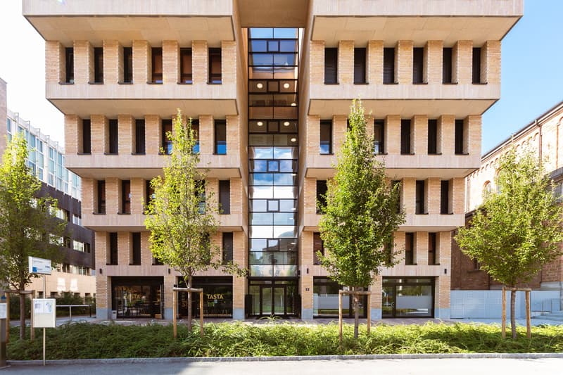 4 story brick building, large glass windows, entrance with double doors, trees in front