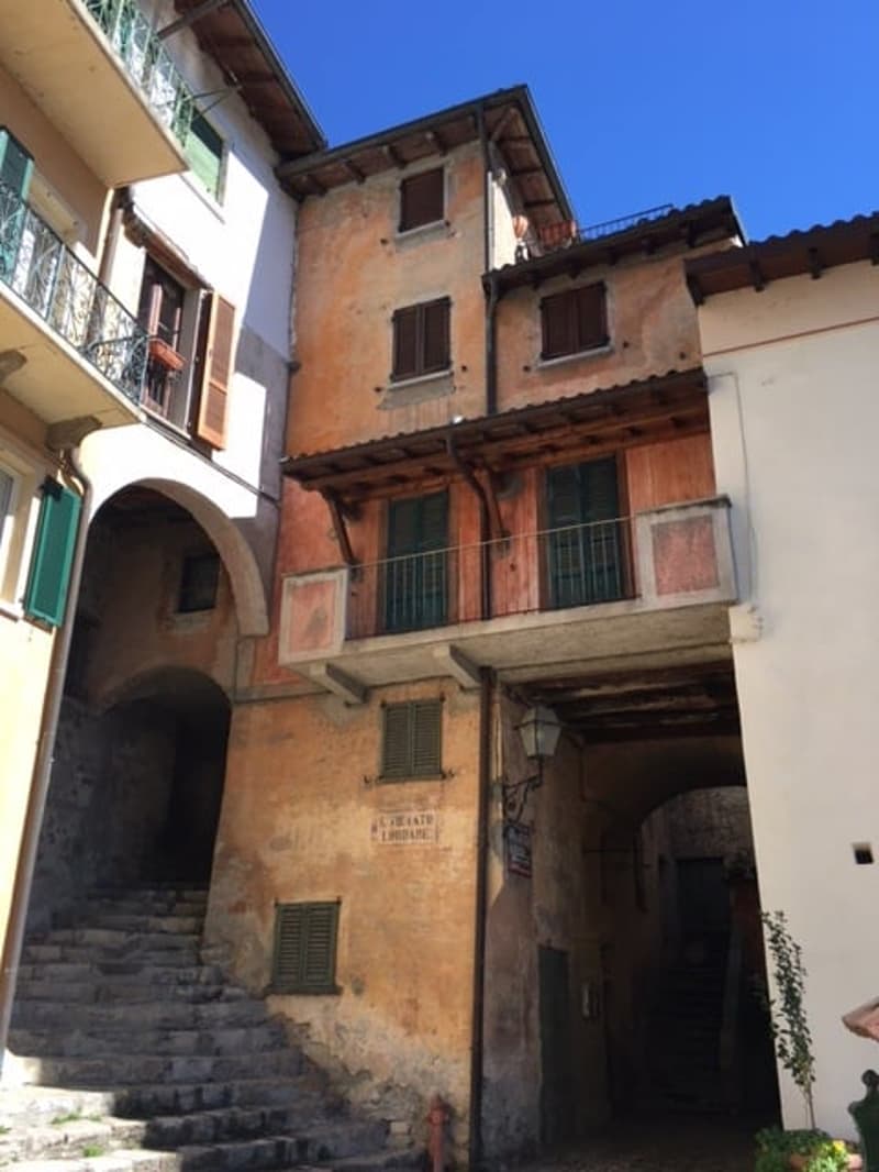 Old, multi-story building with a stone facade, wooden beams, and arched entryway. The building appears to be in a historic or traditional architectural style, typical of an Italian town or village.