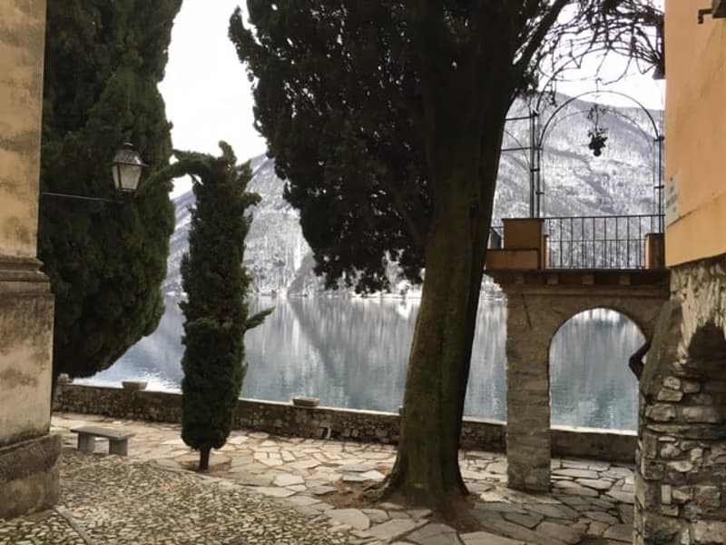 The image shows a picturesque outdoor scene with a canal or body of water surrounded by trees and stone arched structures. The scene has a serene and tranquil atmosphere, with the water reflecting the surrounding environment. The trees and stone architect
