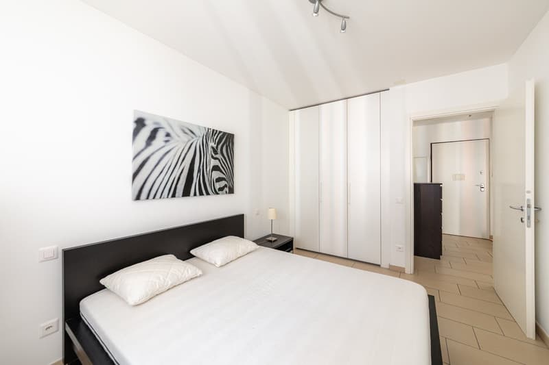 modern bedroom with a double bed, white walls, lamp, framed picture, wardrobe, tiled floor