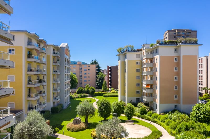 Three-story residential complex with balconies and terraces, manicured garden, and paved walkway.