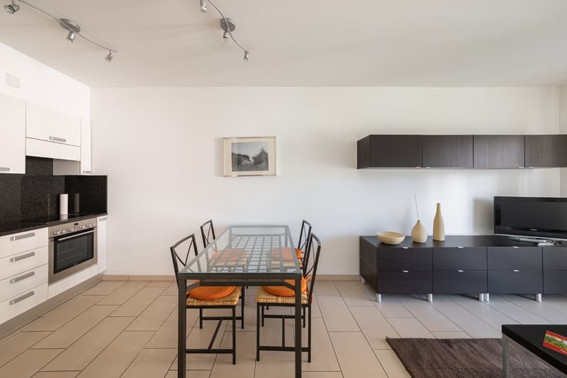 modern dining room with glass table, chairs, white cabinets, tiled floor, black kitchen area, oven, counter, picture frame, TV