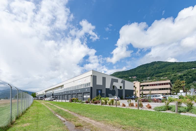 Industrial building with large parking lot, multiple windows, and a sign reading 'H51' on the side.