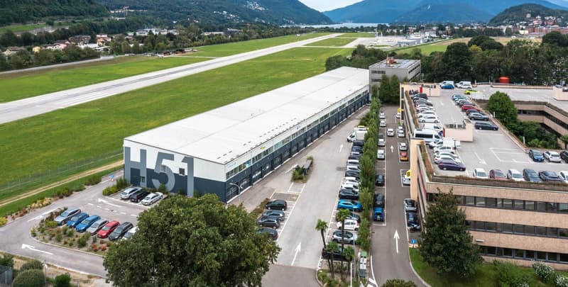 Large industrial building with parking lot, runway in the background