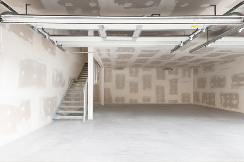 Empty garage with unfinished walls, concrete floor, metal stairs, and ceiling lights