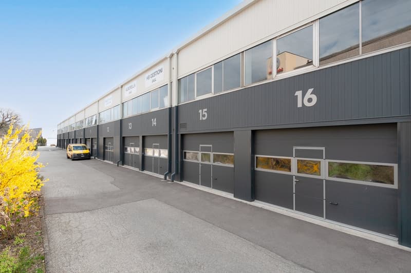 Industrial building with multiple garage doors, yellow van parked in front, gray exterior, glass windows, number 16 on the right side