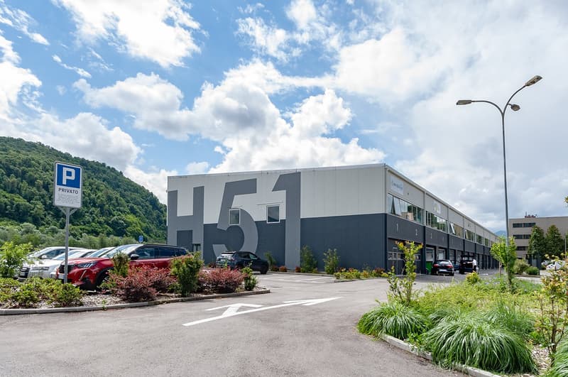 Large building with parking lot, number 151 on the side, surrounded by greenery