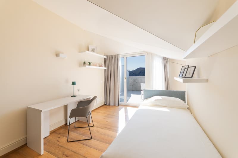 small bedroom with desk, chair, bed, and window with balcony view