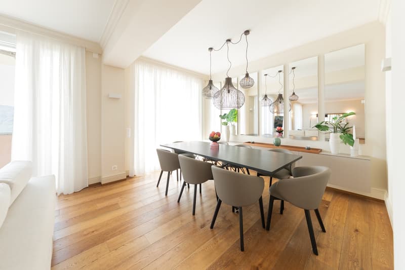 Dining room with wooden floor, large dining table, 6 chairs, pendant lights, white walls, white curtains, mirrors, plants