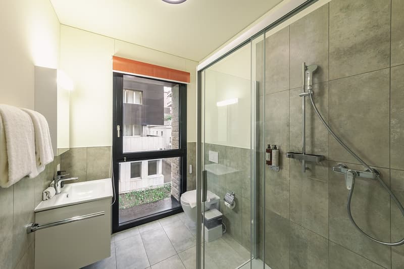 modern bathroom with glass shower, white sink, toilet, and towel rack