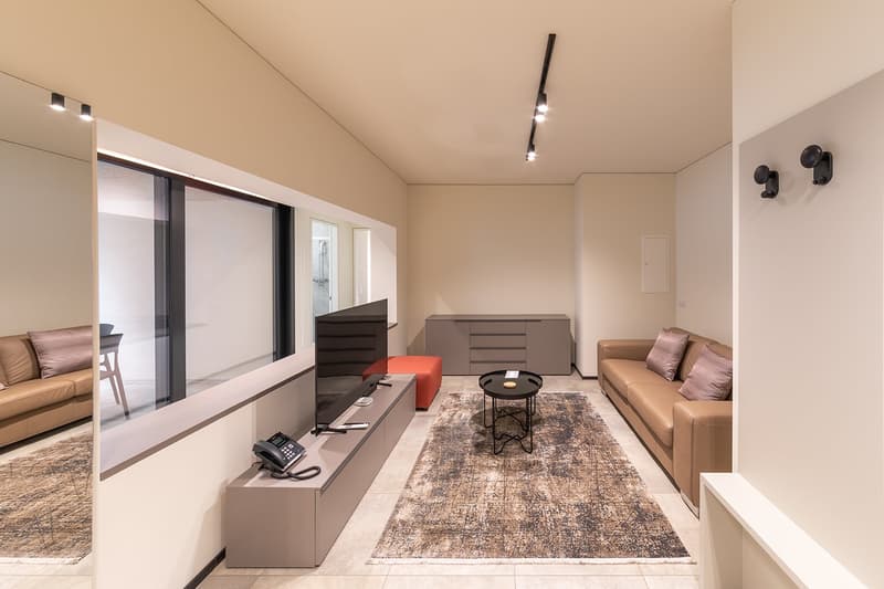 modern living room with beige walls, large windows, beige couch, TV, coffee table, rug, telephone