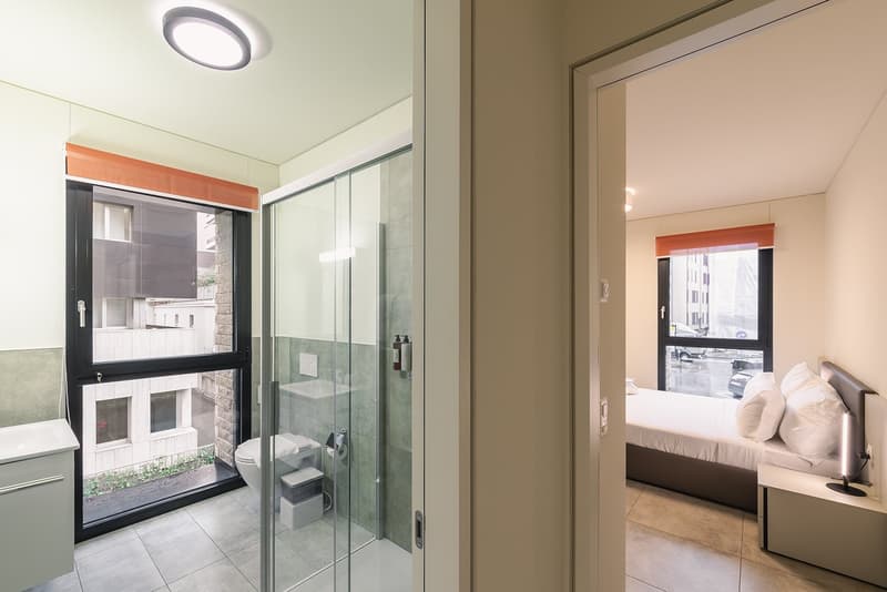 Bathroom with glass shower, toilet, sink, and large window with city view