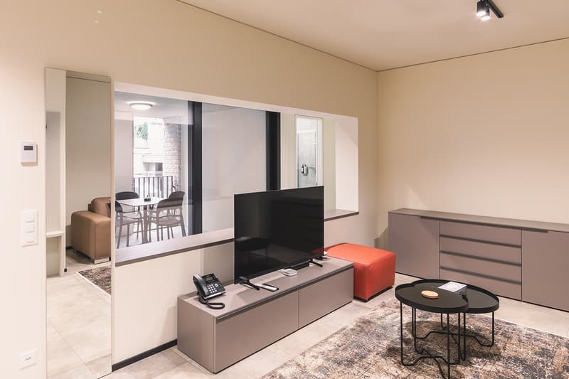 modern living room with large windows, flat screen TV, telephone, ottoman, coffee table, sideboard, carpet