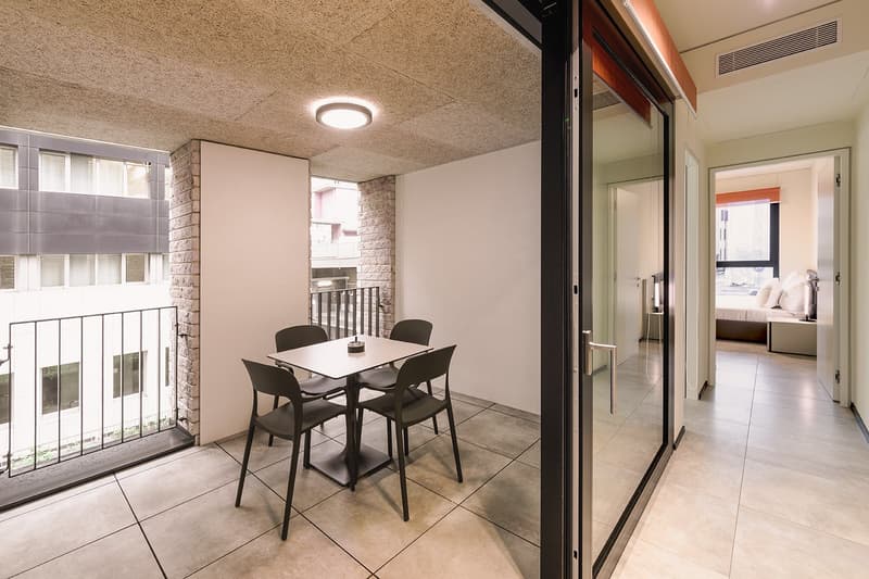 Dining area with table and chairs, balcony with railing, modern interior design, white walls, ceiling light