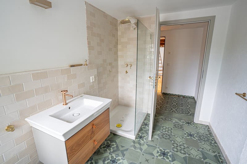 A bathroom with a white sink, tiled walls and floors, a shower with glass doors, a wooden cabinet with drawers, and a white ceiling.