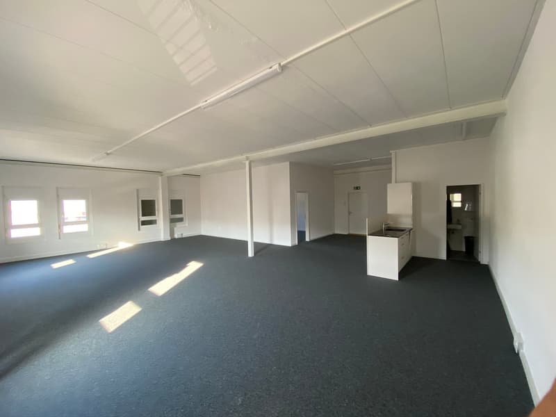 Empty room with white walls, black floor, multiple windows, white kitchen cabinet with sink, door to bathroom