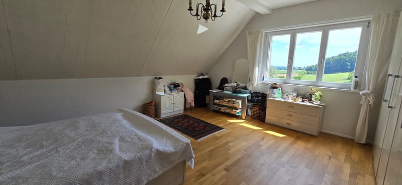 large bed, white blanket, wooden floor, window, desk with books, chair, cabinet, white walls, large mirror, chandelier