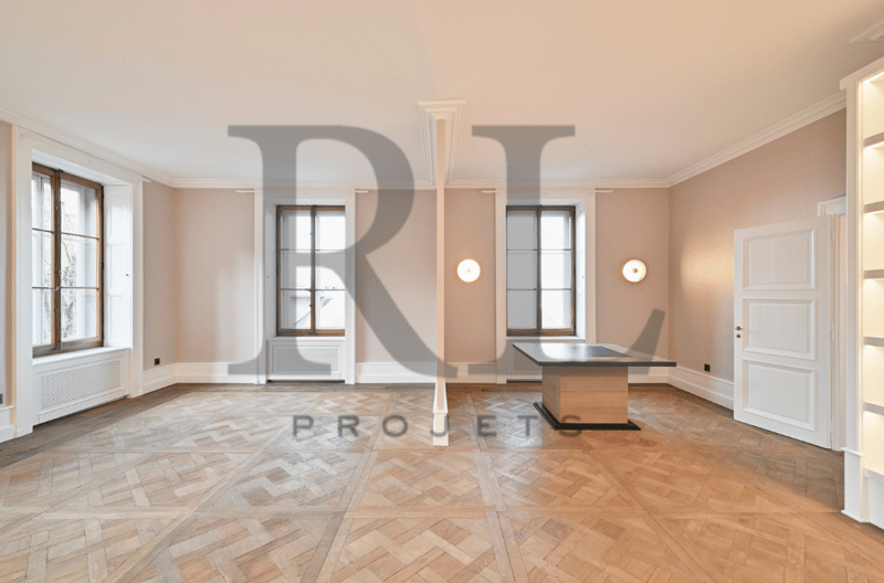 Spacious living room with hardwood flooring, large windows, and a fireplace. The room has a minimalist design with a wooden table in the center.