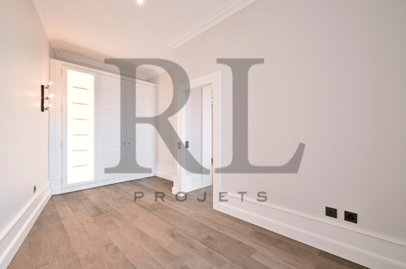 Spacious bedroom with hardwood flooring, white walls, and large windows providing natural light. The room appears to be part of a residential property.