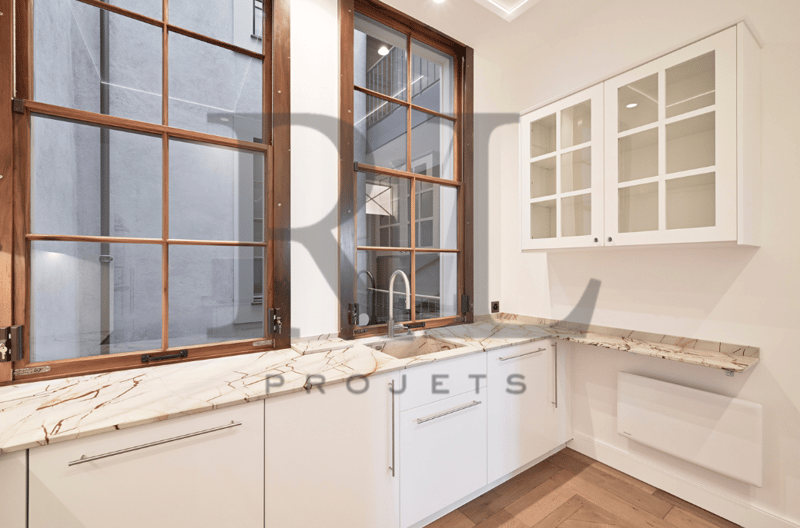 Spacious kitchen with wooden framed windows, white cabinets, marble countertops, and a dishwasher