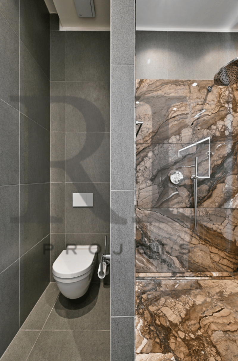 Bathroom with grey tile walls, toilet, and a stone accent wall with a shower fixture