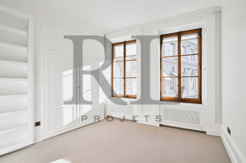Spacious room with white walls, large windows with wooden frames, and hardwood flooring. The room appears to be empty, ready for furnishing and decorating.