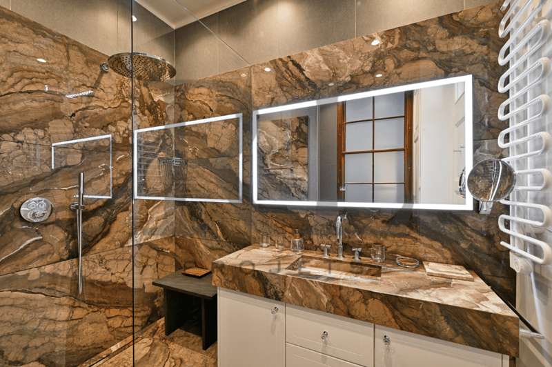 Large bathroom with stone walls, double vanity with marble countertop, large mirror, and a glass-enclosed shower area