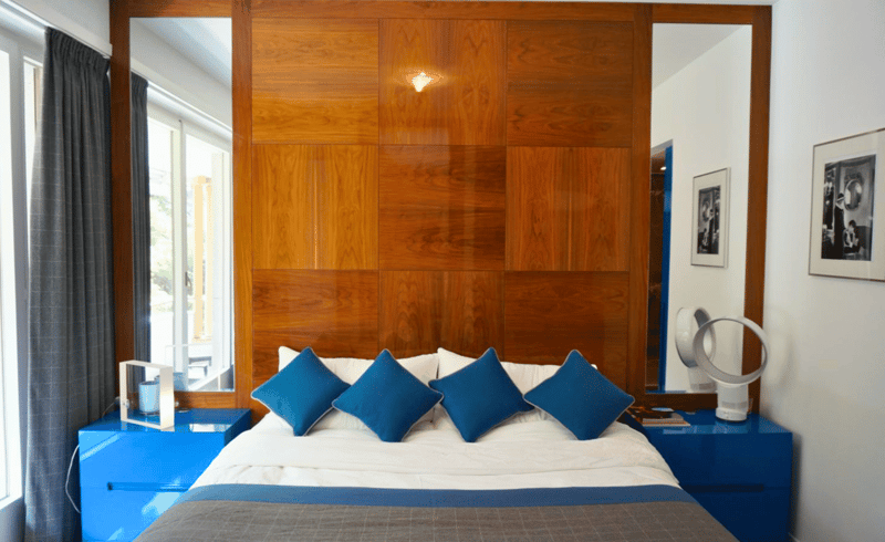 large bed with blue pillows, wooden wall, blue nightstands, mirror