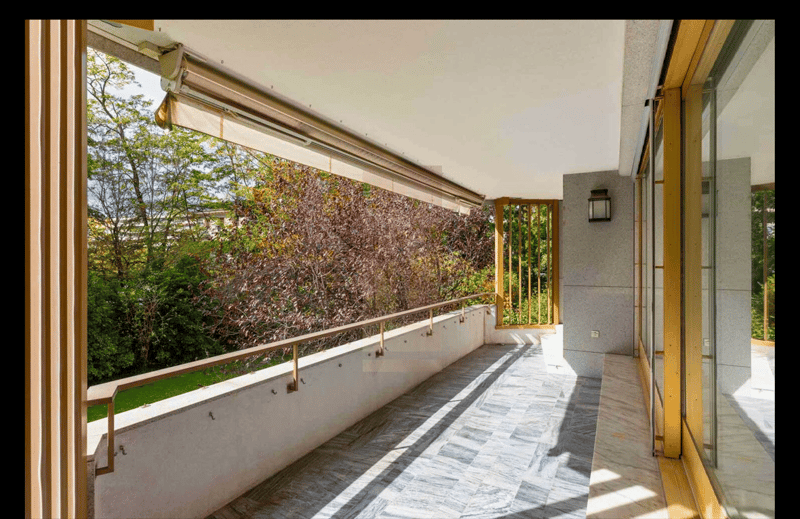 ample balcony with metal railings, shaded by an awning, tiled floor, view of greenery, golden railings