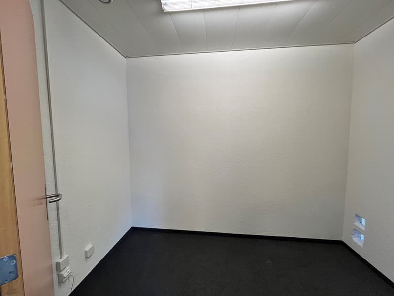 empty room, white walls, black floor, wall-mounted power outlets, small windows, overhead lighting