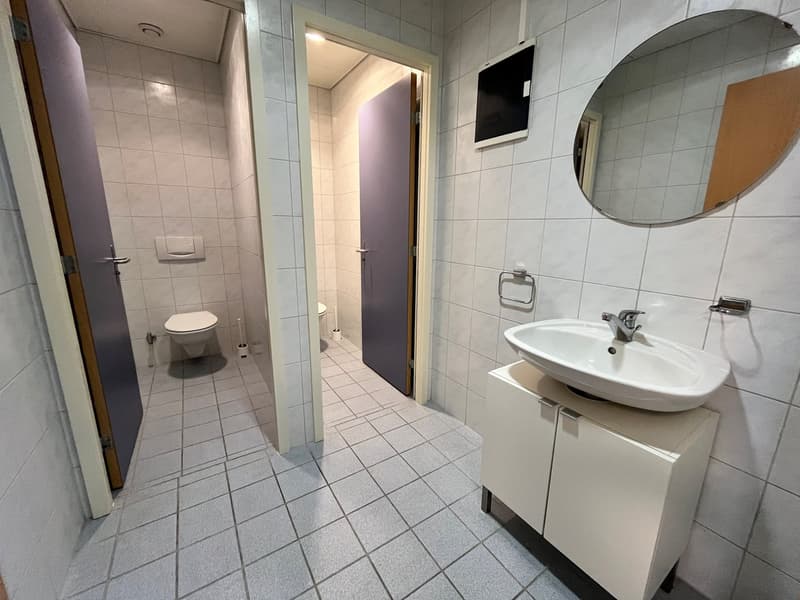 white tiled walls, white sink, large mirror, toilet, shower enclosure, vanity with cabinet