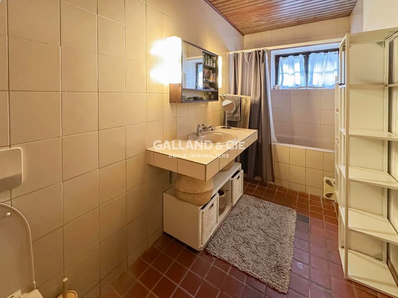 Bathroom with sink, toilet, shelves, rug, and bathtub. Tiled walls and floors.