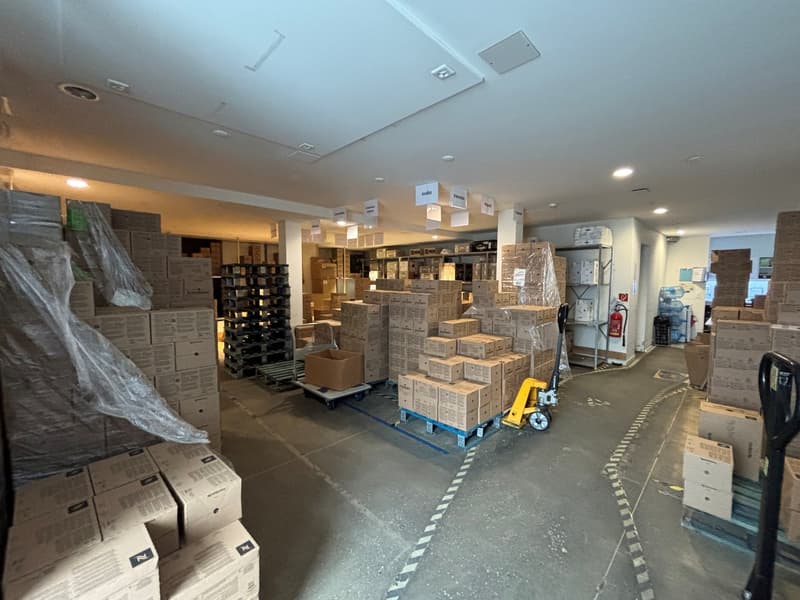 storage area with many boxes stacked on pallets, fire extinguishers present, trolleys, a shelving unit with storage boxes