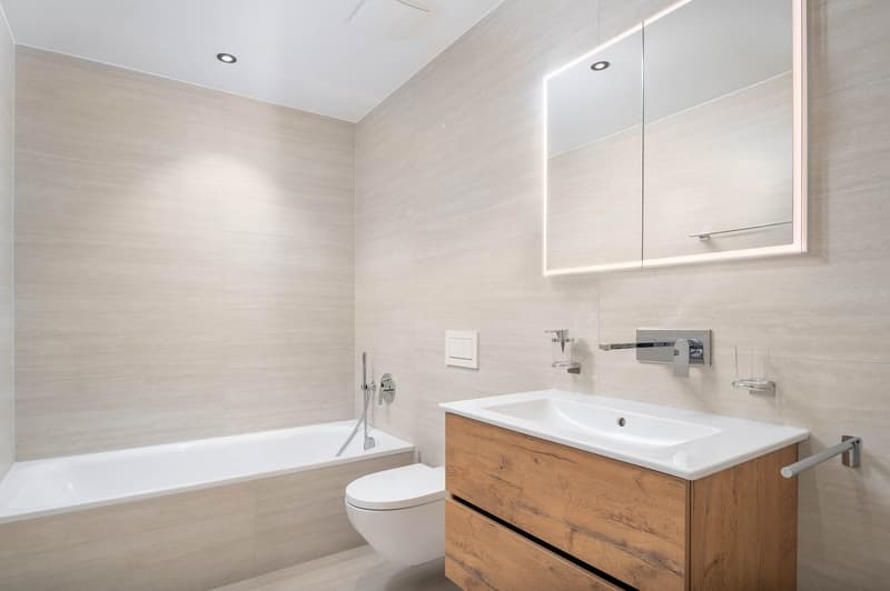 modern bathroom with bathtub, toilet, sink, wooden cabinet, mirror, beige tiles