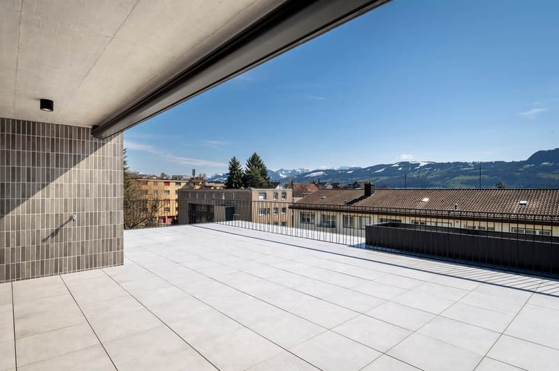 large balcony, tiled floor, black railing, city view, mountains in the distance