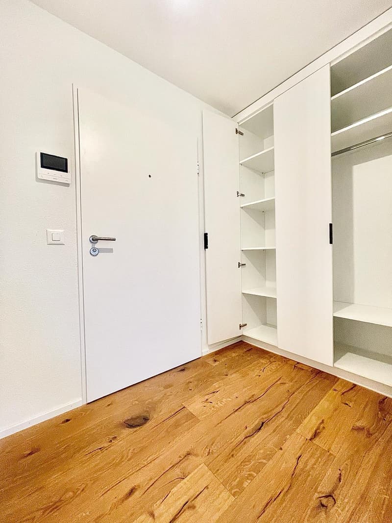 Empty room with wooden floor, white walls, white wardrobe with shelves, door with lock and switch