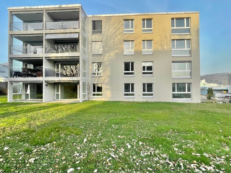 Modern apartment building with multiple balconies, glass windows, and a spacious lawn in front